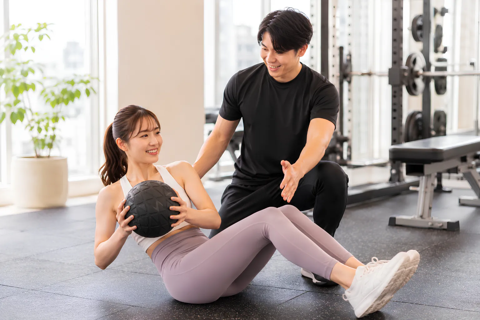 トレーナーとメディシンボールを使った体幹トレーニングを行う女性